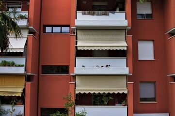 A red colored reinforced concrete residential building with white balconies and awnings (Marche, Italy, Europe)