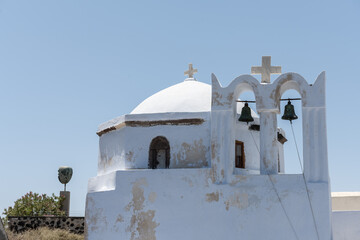 church with two bells White and blue top of buildings in Pyrgos Santorini, Greece with blue sky in a sunny warm day in July 2021.