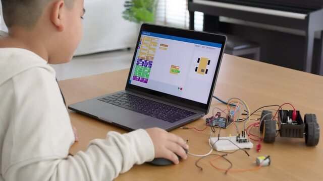 Close-up rear view of young asia teen people sitting at home remote learn online tutor training course at desk table enjoy making electrical robot build cable car. Kid boy play in fun upskill class.