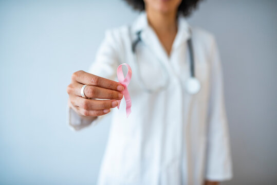 Doctor Hands Holding Pink Cancer Awareness Ribbon. Doctor with pink ribbon on color background, closeup. Breast cancer awareness concept. Cancer awareness concept