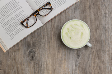 Matcha latte on a wooden surface with a book and reading glasses.