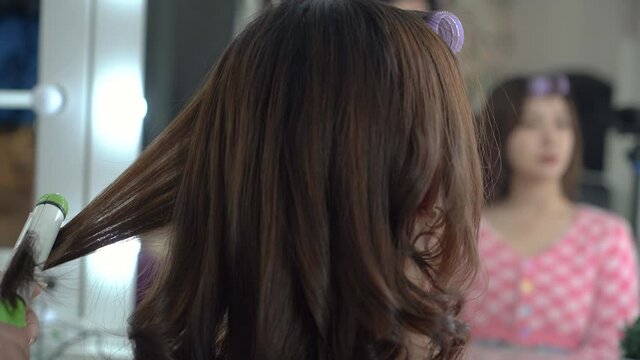 Young hairstylist makes Asian female clients using curling irons (Chinese, Japanese, Korean or Thai). The quarantine is over.