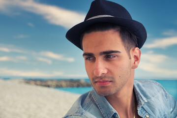 Handsome young, man in denim shirt and fedora hat sitting at beach