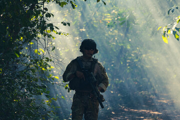 At a natural background, an army soldier in combat uniforms with an assault rifle or gun.