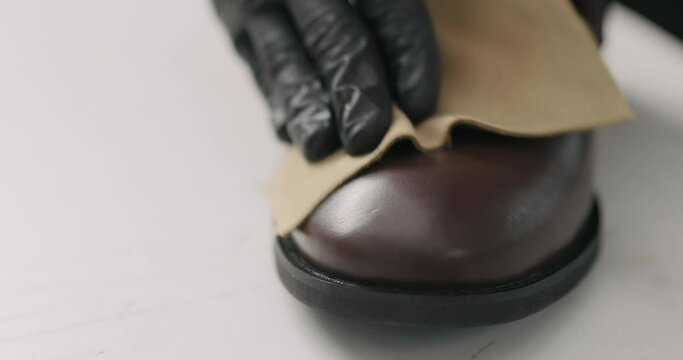 Slow motion man hands in black gloves polishing brown leather chukka boots with cloth