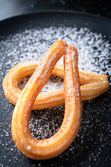 Dark dish with churros sprinkled with sugar. Typical Spanish sweet. Sweet breakfast option