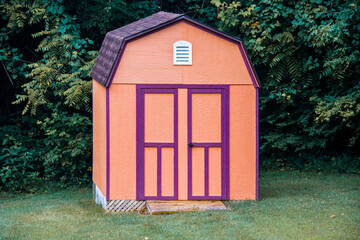 Attractive orange storage shed trimmed in purple sitting in front of lush greenery and trees