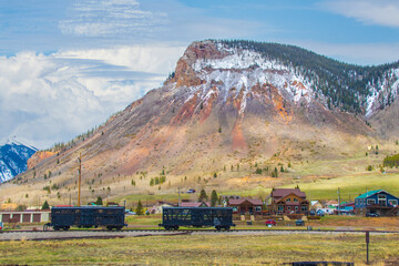 Train cars on track in front of houses in Silverton Colorado with mountains with snow in background.