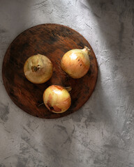 Onions on a wooden board on a concrete background in the rustic style. Top view