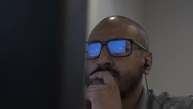 Ethnic Minority Bald Bearded Male In Office, Wearing Glasses And Earphones, Hand On Chin. Locked Off, Low Angle