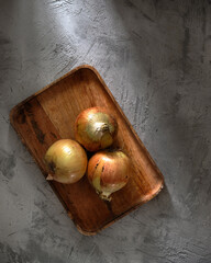 Onions on a wooden tray on a concrete background in the rays of light. Top view