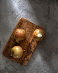 Onions on a wooden board on a concrete background in the rays of light. Top view