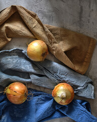 Onions on a concrete background in the rays of light on old napkins. Blue Orange
