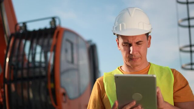 worker in hard a hat with digital tablet near excavator. construction site driver with digital tablet. industry construction concept. worker in hard hat near excavator business truck in uniform.