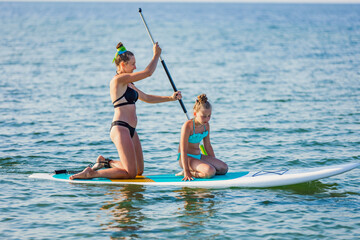 mom and daughter float on the water on a big board