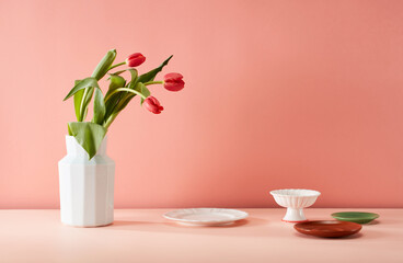Fresh floral arrangement in vase and tableware on pink background