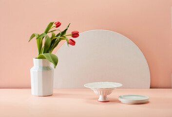 Fresh floral arrangement in vase and tableware on pink background