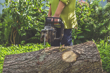 Obraz premium the girl child in a helmet with an electric saw saws a log
