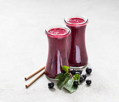 Black currant smoothie in a glass bottle with a bamboo straw on a light gray background