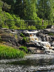 Naklejka na ściany i meble A picturesque waterfall on the Tokhmayoki River in Karelia surrounded by trees on a clear summer morning.