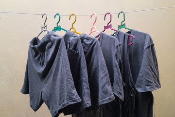 T-shirts and shorts are dried in the sun using colorful clothes hangers with a brown wall background.