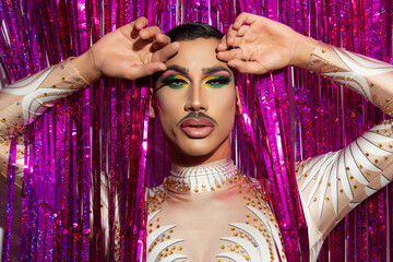 portrait of beautiful young man in drag queen makeup looking at camera and colorful background