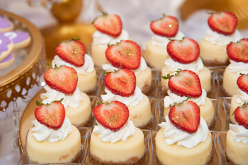 strawberry mini cheesecake in a row. Decorated with cream, a slice of fresh strawberry on top and edible golden glitter.