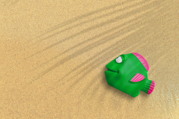 Top up view of green rubber fish on sand beach. vacation concept background.