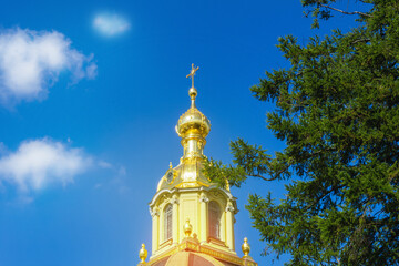Fototapeta na wymiar Golden top of a Christian Orthodox church, dome and cross against blue sky with white clouds and branches of green coniferous tree