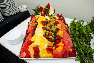 Tray filled with fresh fruit setup on a white table with greenery on the side.