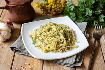 Vegetarian lunch: vegetable noodles with cheese and herbs on a white plate on a wooden table. Zucchini pasta with parmesan on a beautiful plate. Close-up