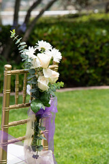 Upper part of a golden chair decorated wit white flowers setup outdoors.