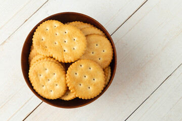Rounded cracker cookies in a wooden bowl on white wooden table background.