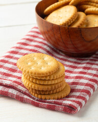 Rounded cracker cookies in a wooden bowl with tablecloth on white wooden table background.