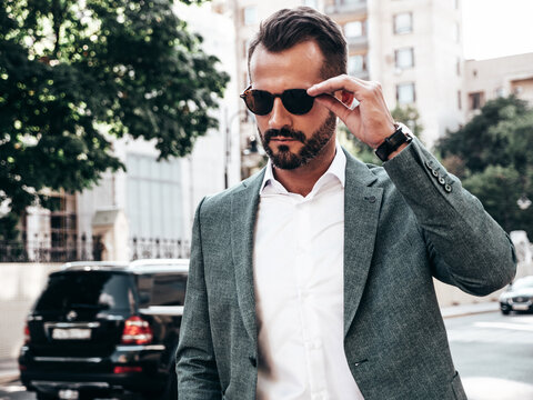 Portrait of handsome confident stylish hipster lambersexual model.Modern man dressed in elegant suit. Fashion male posing in the street background in Europe city at sunset. In sunglasses