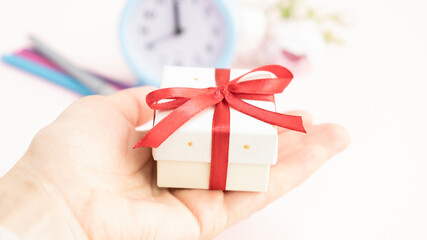A girl holds a gift wrapped in craft paper with a red bow on a white background. Close-up, space for text.