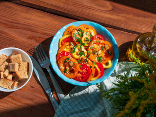 Yellow red tomatoes and sweet pepper salad in blue ceramic bowl breakfast top view. Fresh flower and colorful vegetables mixed sliced greens olive oil vinegar pumpkin sesame flax seeds on wooden table