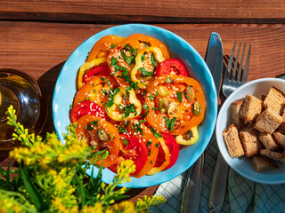 Yellow red tomatoes and sweet pepper salad in blue ceramic bowl breakfast top view. Fresh flower and colorful vegetables mixed sliced greens olive oil vinegar pumpkin sesame flax seeds on wooden table