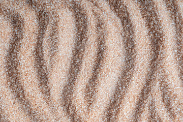 Background or backdrop of texture of brown cane sugar containing molasses with curved lines pattern used in baked goods, confectionery, and toffees. Also looks like sand from the beach. Horizontal
