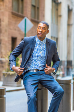 Unbuttoning his jacket, a young black businessman is sitting on the street and taking a break.