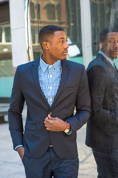 A young black businessman is standing by a mirror and looking at the reflection.