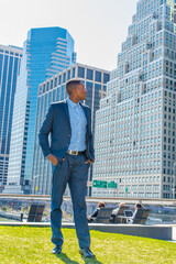 A young black businessman is standing in the front of a busy business district, looking around and taking a break..