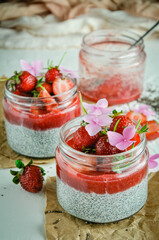 Healthy strawberry fruit dessert with milk and chia seeds in jar on light background. Healthy raw vegetarian dessert.