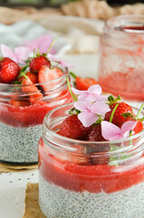 Healthy strawberry fruit dessert with milk and chia seeds in jar on light background. Healthy raw vegetarian dessert.