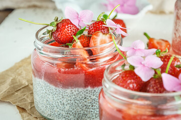 Healthy strawberry fruit dessert with milk and chia seeds in jar on light background. Healthy raw vegetarian dessert.