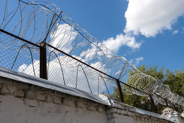 Prison fence with barbed wire on a background of blue sky with clouds