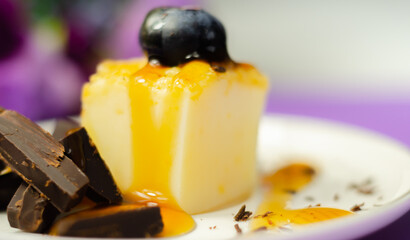 A portion of vanilla cheesecake decorated with blueberries and pieces of milk chocolate, topped with caramel sauce