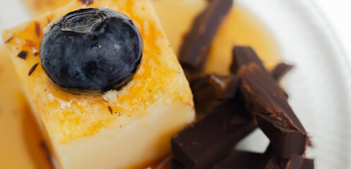 A portion of vanilla cheesecake decorated with blueberries and pieces of milk chocolate, topped with caramel sauce