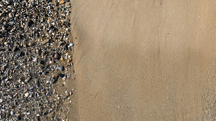 Beach sand with small stones and sea foam in beautiful coast