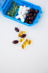 Spilling pills and capsules on a white background close-up together with a container for pills. Top view with copy space. Medicine concept.